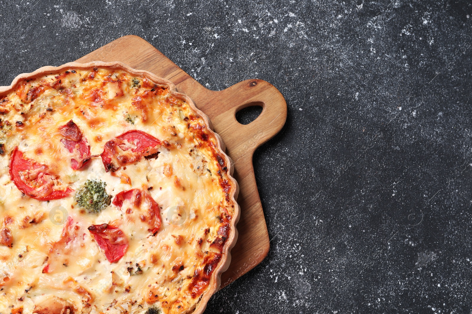 Photo of Tasty quiche with tomatoes and cheese on dark textured table, top view. Space for text