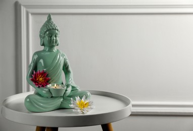 Buddha statue with burning candle and lotus flowers on white table. Space for text