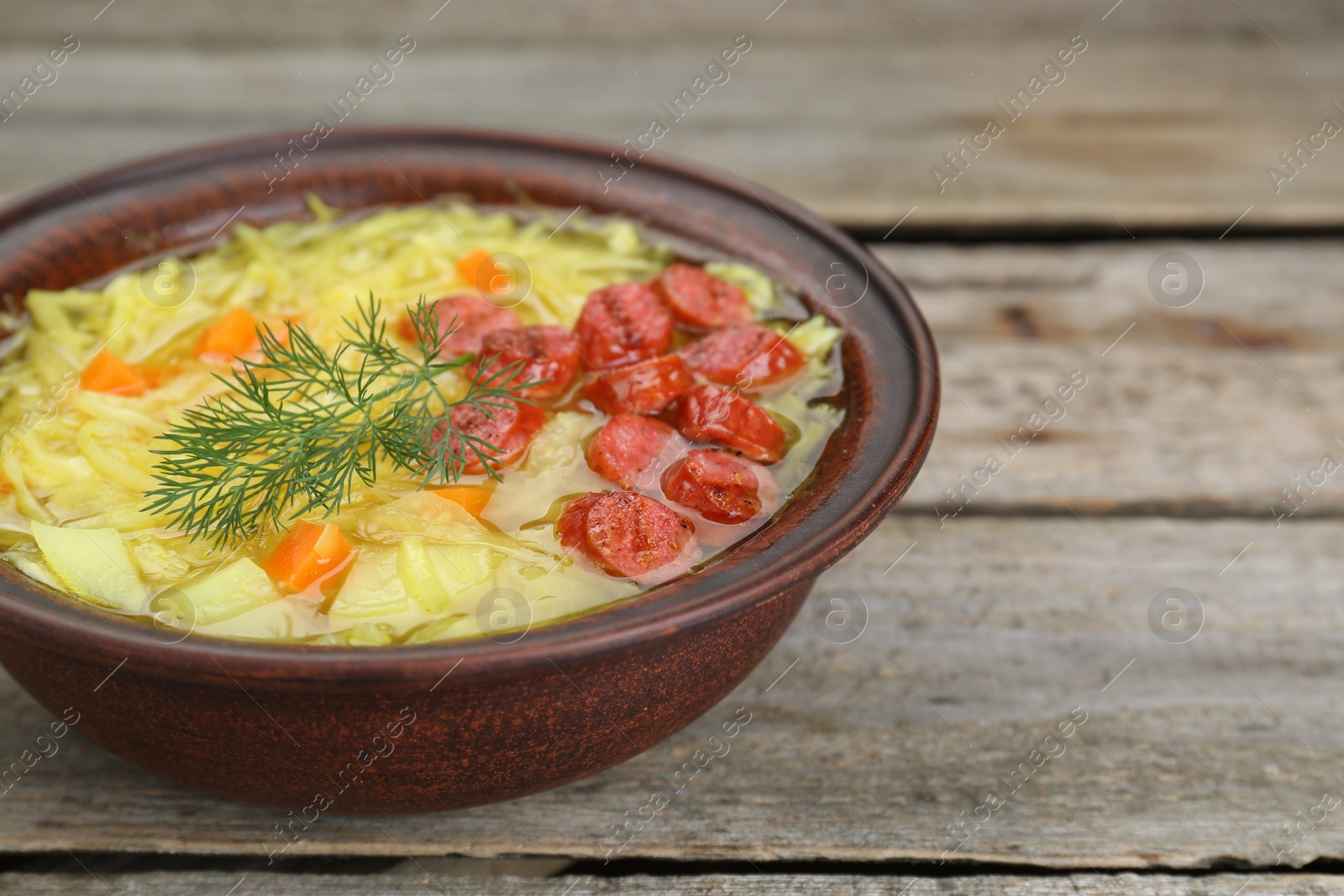 Photo of Bowl of delicious sauerkraut soup with smoked sausages and dill on wooden table, closeup. Space for text