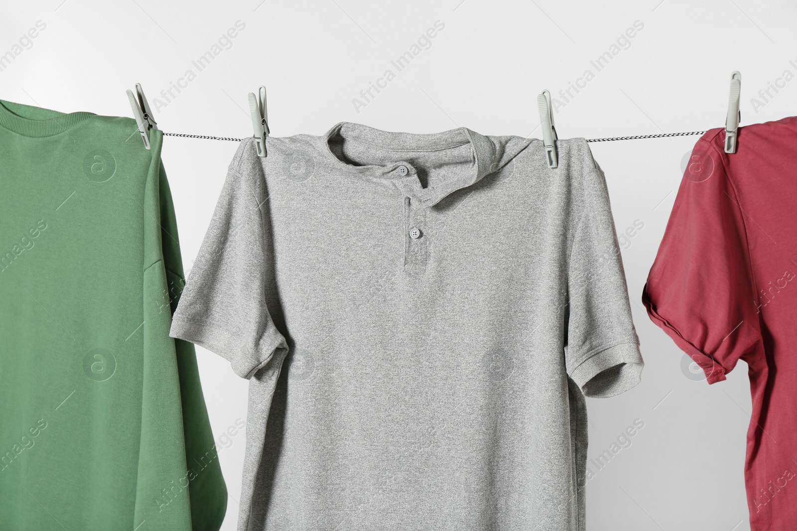 Photo of Different shirts drying on laundry line against light background, closeup