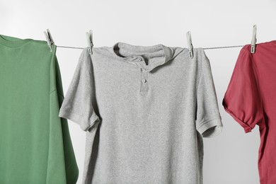 Photo of Different shirts drying on laundry line against light background, closeup