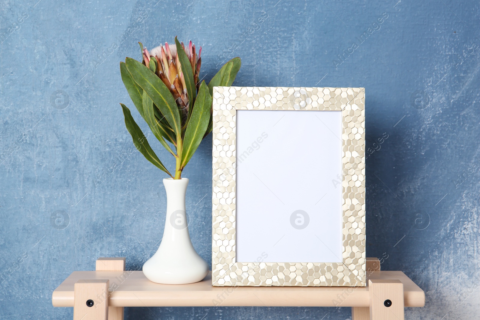 Photo of Blank frame and vase with flower on table near color wall. Mock up for design