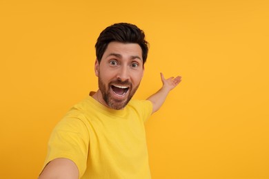 Photo of Happy man taking selfie on yellow background, space for text