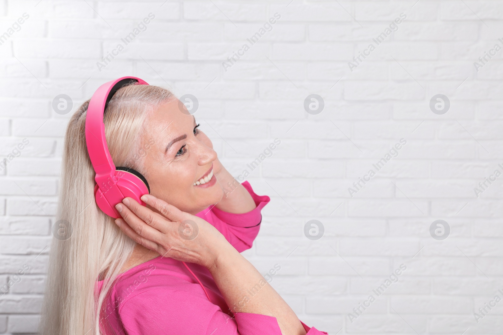 Photo of Mature woman enjoying music in headphones against brick wall. Space for text