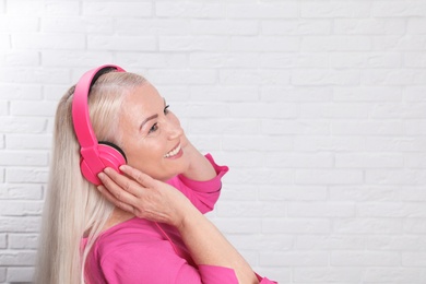 Mature woman enjoying music in headphones against brick wall. Space for text