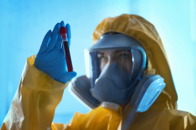 Photo of Scientist in chemical protective suit holding test tube with blood sample at laboratory, focus on hand. Virus research