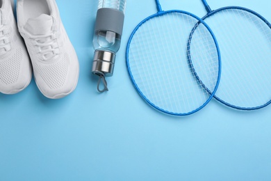 Photo of Badminton rackets, bottle and shoes on light blue background, flat lay. Space for text