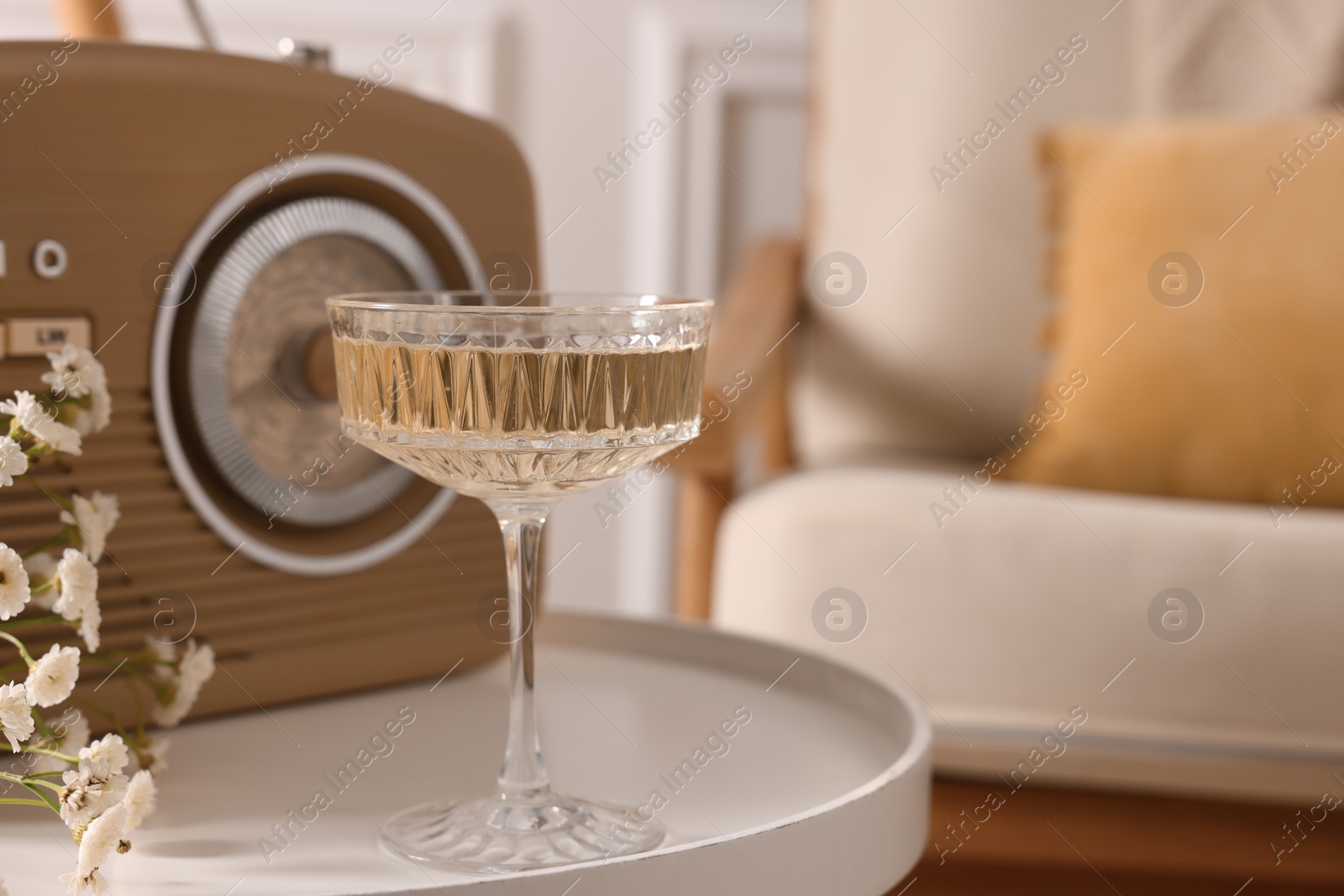 Photo of Glass of alcohol drink, flowers and radio set on table in room, closeup and space for text. Relax at home