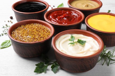 Photo of Many different sauces and herbs on white wooden table, closeup