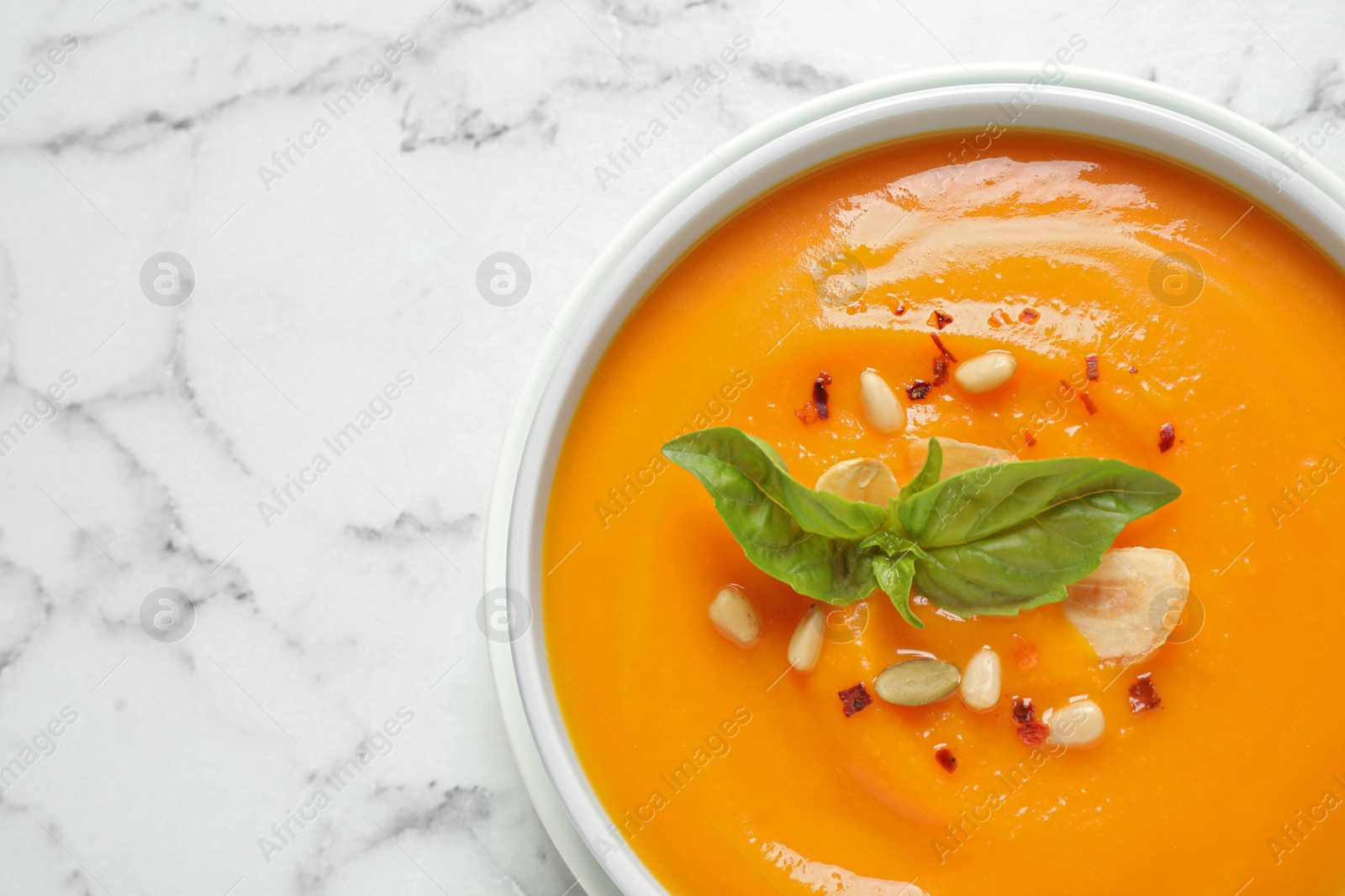 Photo of Delicious pumpkin soup in bowl on marble table, top view. Space for text