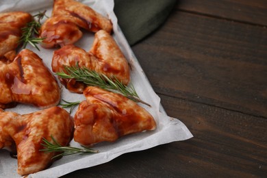 Photo of Raw marinated chicken wings and rosemary on wooden table, closeup. Space for text