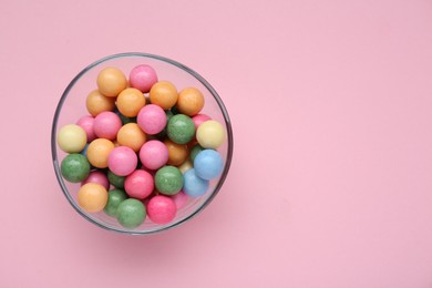 Photo of Bowl with many bright gumballs on pink background, top view. Space for text