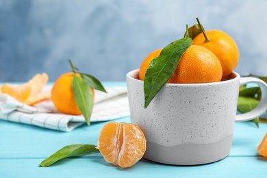 Photo of Fresh ripe tangerines with green leaves and mug on table. Space for text