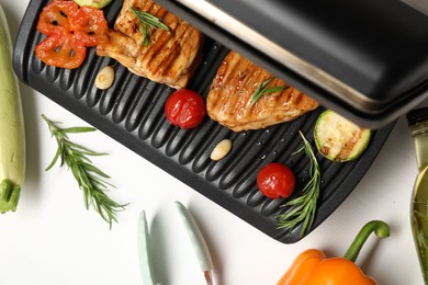 Photo of Electric grill with tasty meat, spices and vegetables on white table, flat lay