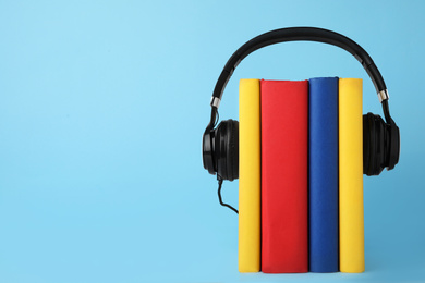 Photo of Books and modern headphones on light blue background. Space for text