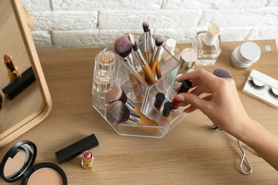 Woman taking cosmetics from organizer for makeup products on table