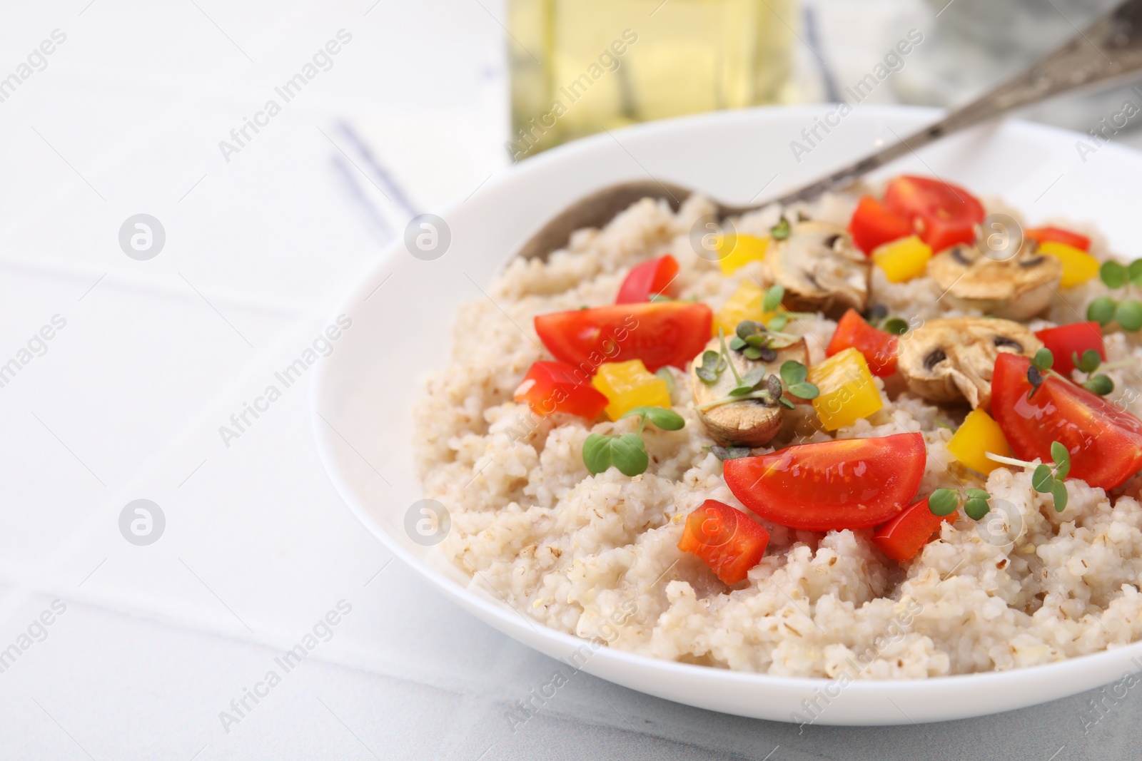 Photo of Delicious barley porridge with vegetables and microgreens in bowl on white table, closeup