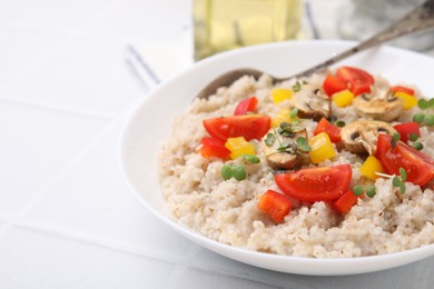 Delicious barley porridge with vegetables and microgreens in bowl on white table, closeup