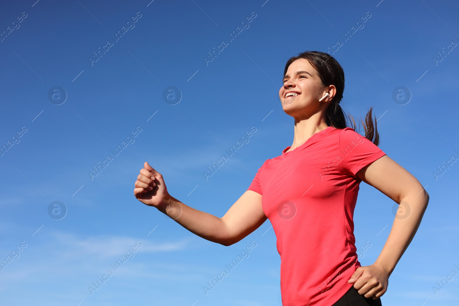 Photo of Young woman listening to music while running outdoors in morning, low angle view. Space for text