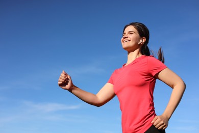 Young woman listening to music while running outdoors in morning, low angle view. Space for text