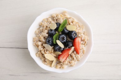 Photo of Tasty oatmeal with strawberries, blueberries and almond petals in bowl on white wooden table, top view