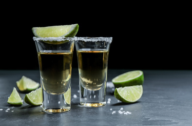 Mexican Tequila shots with salt and lime slices on grey table. Space for text