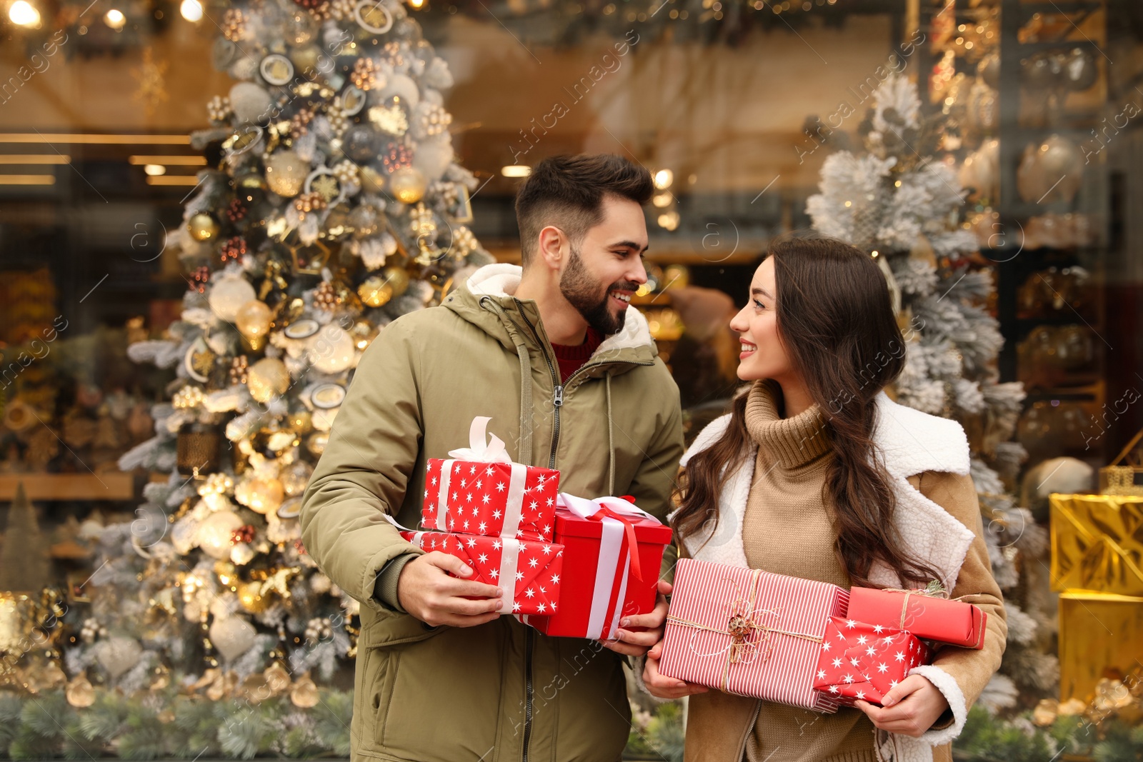 Photo of Lovely couple with presents near store decorated for Christmas outdoors