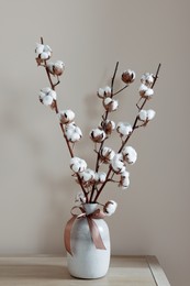 Photo of Vase with beautiful bouquet of white fluffy cotton flowers on wooden table in cozy room