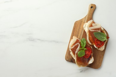Photo of Tasty sandwiches with cured ham, basil and tomatoes on white marble table, top view. Space for text