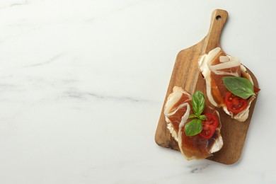 Tasty sandwiches with cured ham, basil and tomatoes on white marble table, top view. Space for text