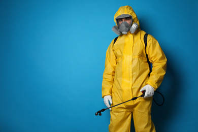 Photo of Man wearing protective suit with insecticide sprayer on blue background, space for text. Pest control