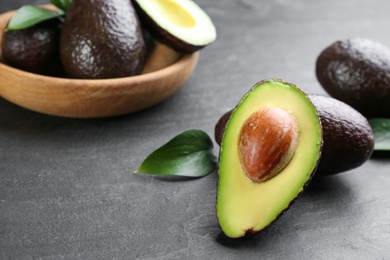 Photo of Whole and cut avocados with green leaves on grey table