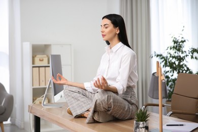 Photo of Young woman meditating at workplace. Stress relief exercise