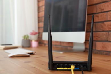 Modern wi-fi router near computer on wooden table