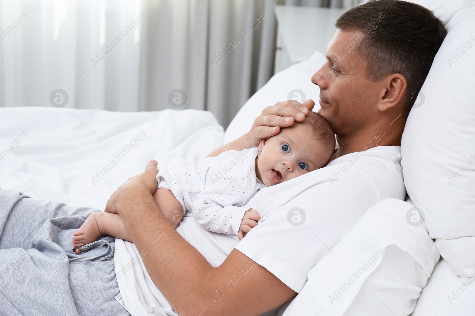 Photo of Happy father holding his cute baby on bed at home