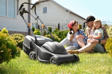 Parents, their daughter and dog spending time in garden, focus on lawn mower