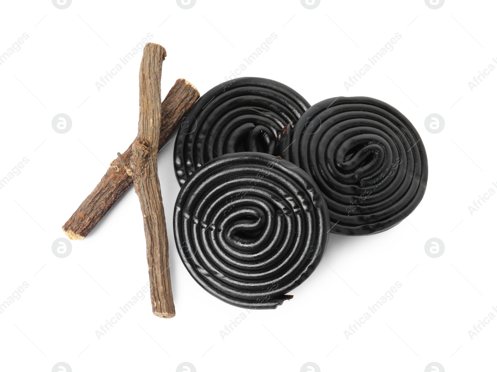 Photo of Tasty black candies and dried sticks of liquorice root on white background, top view