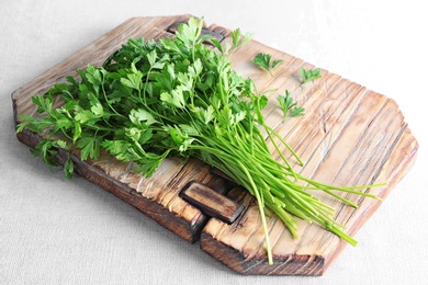 Photo of Wooden board with fresh green parsley on light fabric