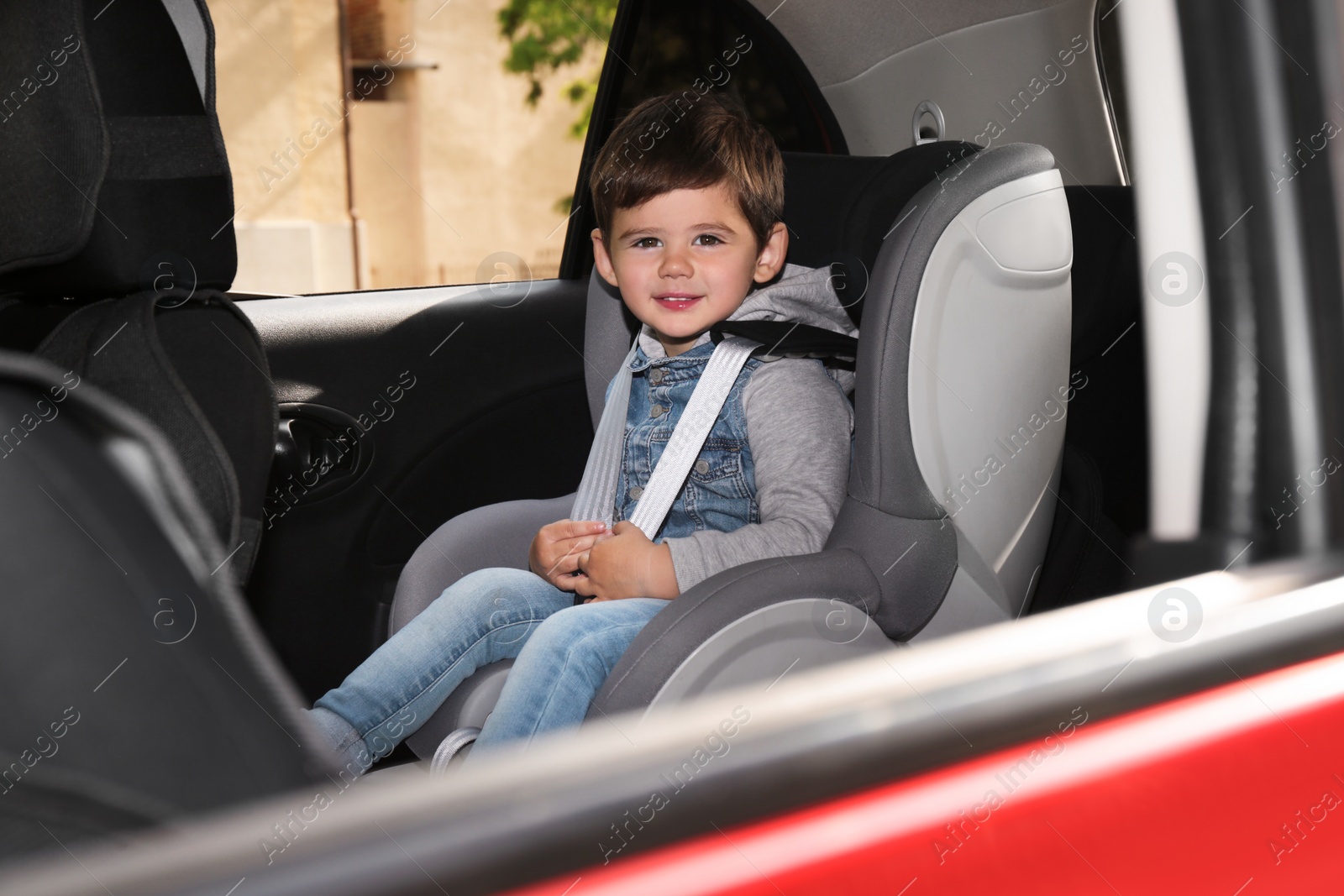 Photo of Cute little child sitting in safety seat inside car. Danger prevention