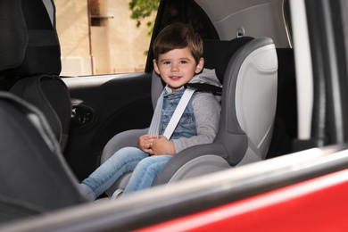 Photo of Cute little child sitting in safety seat inside car. Danger prevention