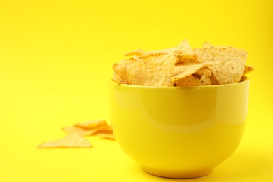 Photo of Bowl of tasty Mexican nachos chips on yellow background. Space for text