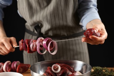 Woman stringing marinated meat on skewer at table, closeup