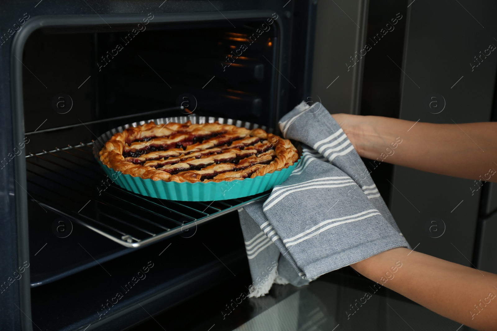 Photo of Woman taking delicious fresh homemade cake out of oven indoors, closeup