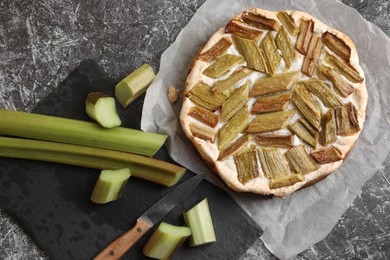 Photo of Freshly baked rhubarb pie, stalks and knife on grey textured table, flat lay
