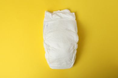 Baby diaper on yellow background, top view