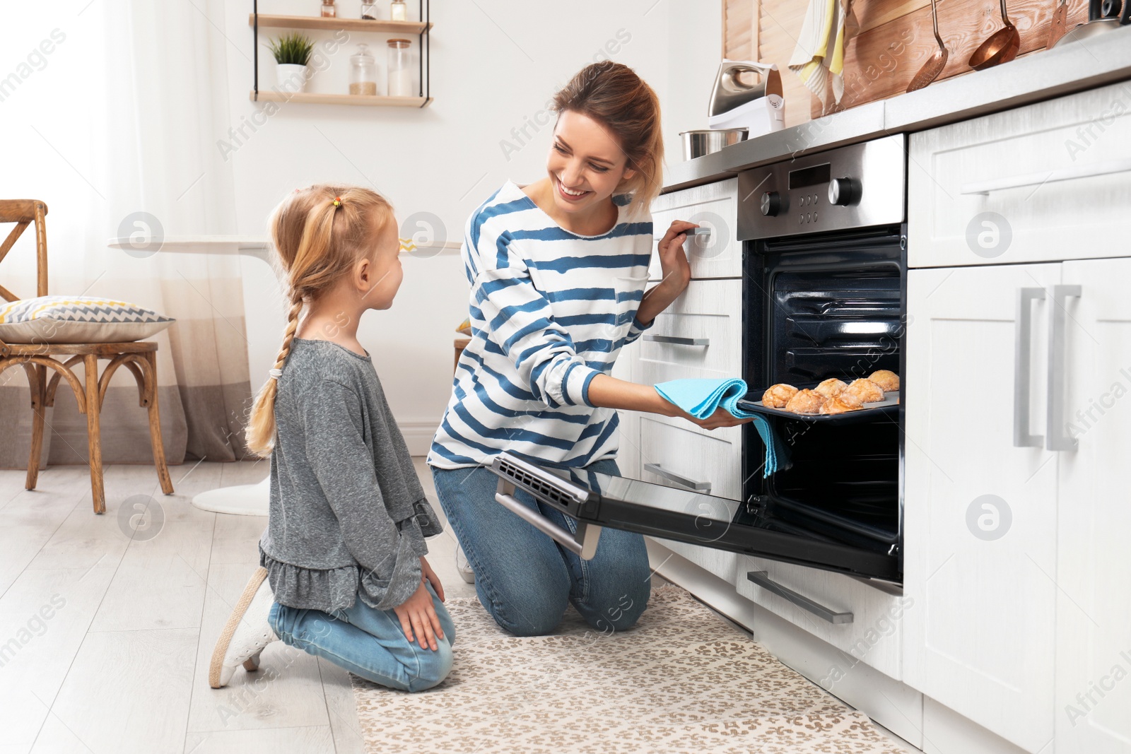 Photo of Mother and her daughter taking out cookies from oven in kitchen