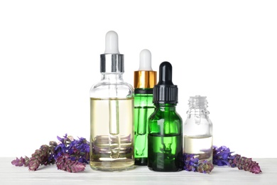 Photo of Bottles of sage essential oil and flowers on wooden table, white background