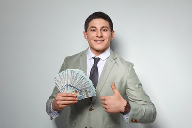 Portrait of young businessman with money fan on light background