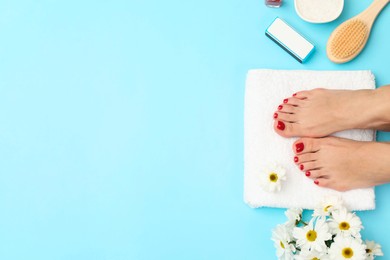 Photo of Woman with stylish red toenails after pedicure procedure and chamomile flowers on light blue background, top view. Space for text