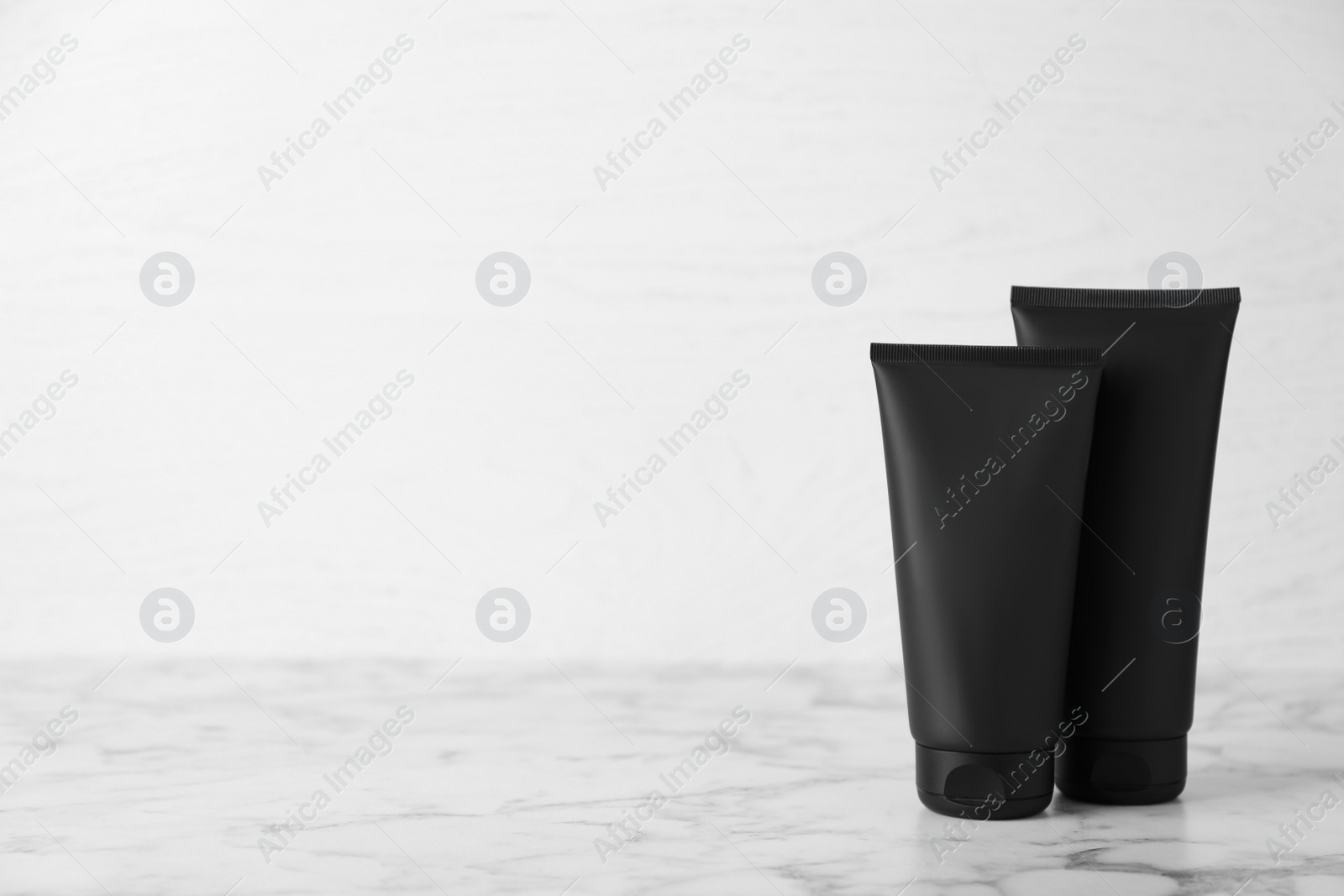 Photo of Tubes of men's facial creams on white marble table. Mockup for design